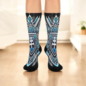Könnte beinhalten: Kniestrümpfe mit einem Schilddesign in Blau, Weiß und Schwarz. Die Socken zeigen ein zentrales Schildemblem mit einem Kreuz, umgeben von detaillierten Mustern. Die Zehen und Fersen sind schwarz.