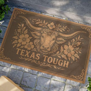 May include: A brown doormat with a floral design and a longhorn steer head. The text "TEXAS TOUGH" is printed on the doormat.