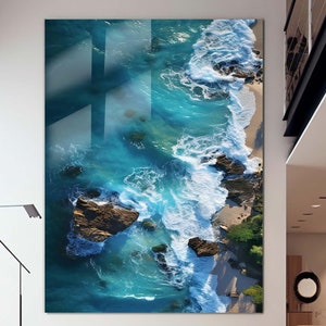 May include: An aerial view of a rocky coastline with turquoise blue water crashing against the shore. The waves are white and foamy, and the rocks are brown and gray.