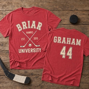 Könnte beinhalten: Zwei rote T-Shirts mit weißem Text und Grafiken. Ein Shirt zeigt "Briar Hawks University" mit gekreuzten Hockeyschlägern. Das andere Shirt zeigt "Graham 44". Ein Hockeypuck und ein Schläger sind ebenfalls zu sehen.