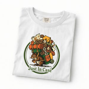 May include: White t-shirt with a graphic of a squirrel carrying camping gear, including a tent, map, and rolled sleeping bags. The text "Just In Case" is printed below the squirrel in a green circle.