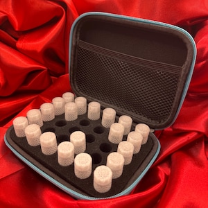 May include: A black zipped storage case with a light blue trim, containing a black foam insert with multiple circular cutouts. Several small, translucent, cylindrical containers with textured, honeycomb-patterned sides are seated in the foam.
