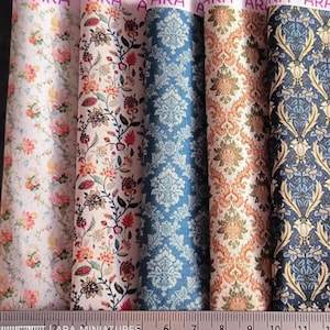 May include: A collection of fabric samples with floral and damask patterns. The fabrics feature a variety of colors, including pink, orange, blue, and navy. A ruler with inch markings is at the bottom. The text "ARA" is visible at the top of the fabrics.
