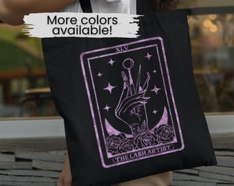 May include: Black tote bag with a purple design of a tarot card featuring a hand holding lash tools. The card reads "The Lash Artist" and "XLV".