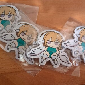 May include: Four white iron-on patches featuring a cartoon girl with blonde hair and wings. The girl is wearing a green shirt and white pants. The patches are on a white background.
