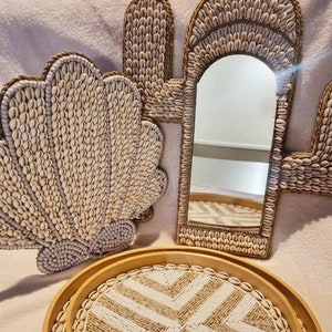 Op de afbeelding: Een set van drie decoratieve schalen gemaakt van natuurlijke materialen. De schalen zijn rond en hebben een geometrisch patroon van witte en beige kralen. De grootste schaal heeft een spiegel in het midden, omlijst door een schelpvormig ontwerp.