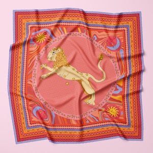 Puede incluir: Un pañuelo de seda cuadrado rosa y naranja con una ilustración detallada de un león en un círculo rodeado de estrellas. El pañuelo tiene un borde azul, naranja y amarillo.