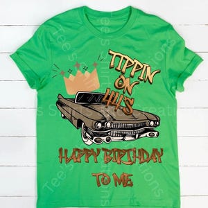 May include: A green t-shirt featuring a brown classic car graphic with the text "Tippin' on 44's" and "Happy Birthday to Me." A brown crown graphic is above the car. The shirt is a short-sleeved crew neck.