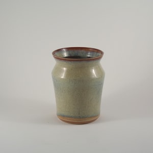 May include: A ceramic vase with a light green glaze and a brown rim. The vase has a slightly flared opening and a rounded bottom.