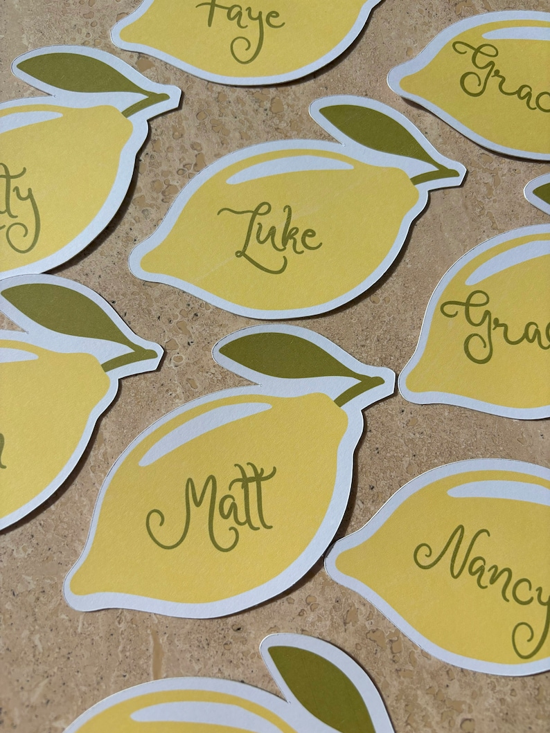 May include: Lemon-shaped place cards with names written in cursive. The names include Faye, Luke, Matt, Nancy, and Grace. The place cards are yellow with green leaves.