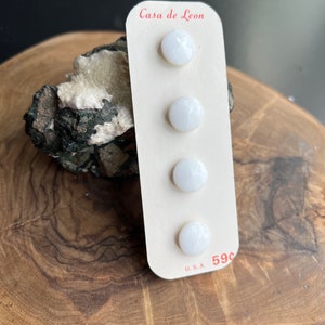 May include: A card with four white buttons on it. The card says "Casa de Leon" and "59c" in red text. The card is on a wooden surface.
