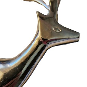 May include: A polished silver-colored deer head sculpture. The deer's head is angled slightly upward, with detailed antlers and a sleek, reflective surface. The sculpture is likely made of metal and is a decorative item.