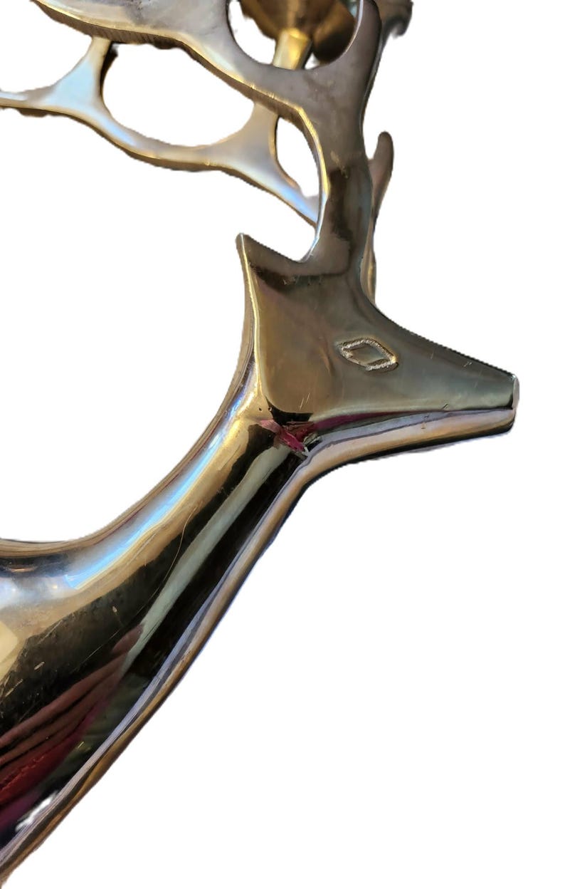 May include: A polished silver-colored deer head sculpture. The deer's head is angled slightly upward, with detailed antlers and a sleek, reflective surface. The sculpture is likely made of metal and is a decorative item.