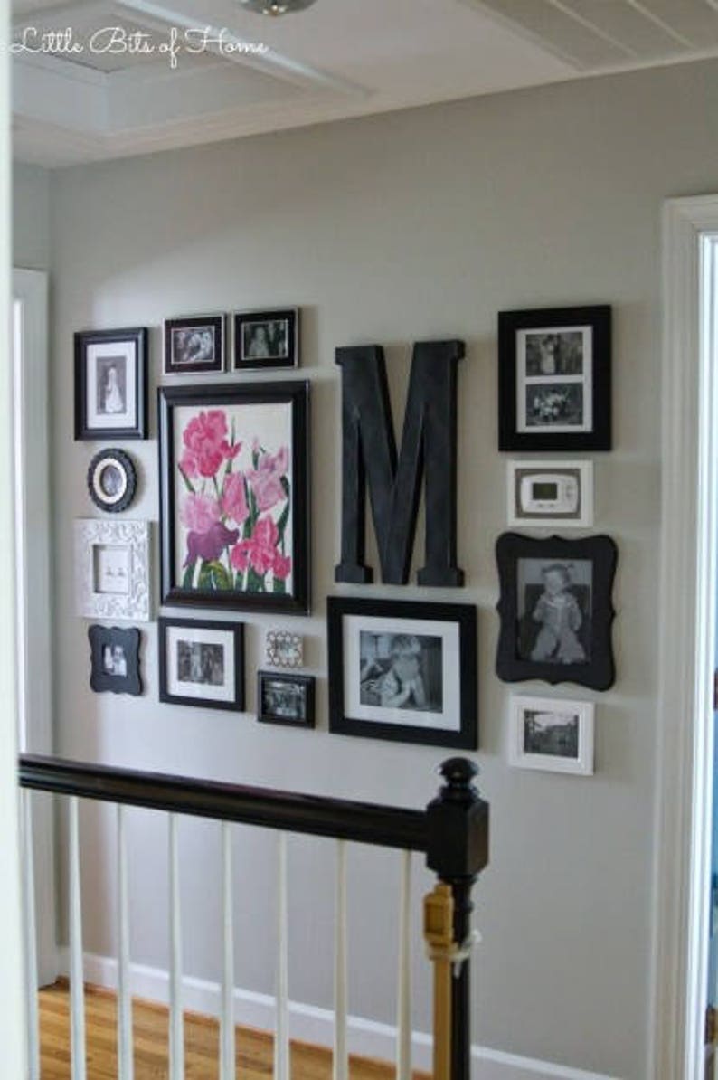 Strong example of an asymmetrical, mostly monochromatic, gallery-style display of black and white framed photos mixed with an oversized black monogram. Frames have either white mats or no mats. One large, colorful floral print with pink and purple.