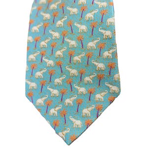 May include: A turquoise tie with a repeating pattern of white elephants and orange palm trees. The tie is made of a woven fabric and has a classic pointed end. The design is a tropical theme.