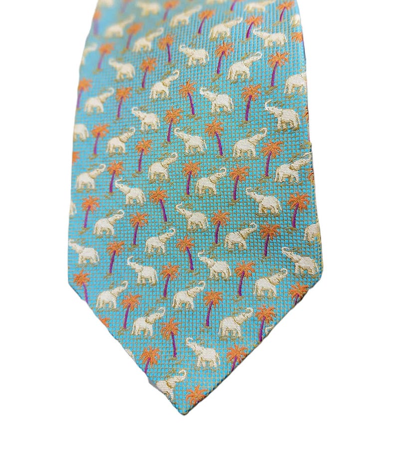 May include: A turquoise tie with a repeating pattern of white elephants and orange palm trees. The tie is made of a woven fabric and has a classic pointed end. The design is a tropical theme.