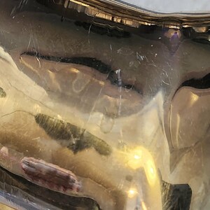 May include: Close-up of a shiny, silver-colored object with a curved shape. The surface reflects light, showing distorted reflections and minor scratches. The object appears to be made of metal, possibly a decorative piece.