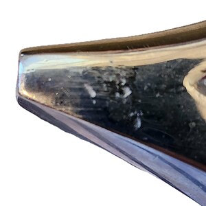 May include: Close-up of a shiny, metallic object with a reflective surface. The object has a dark, possibly blue or black, color with a lighter, possibly silver, edge. The surface shows some imperfections.