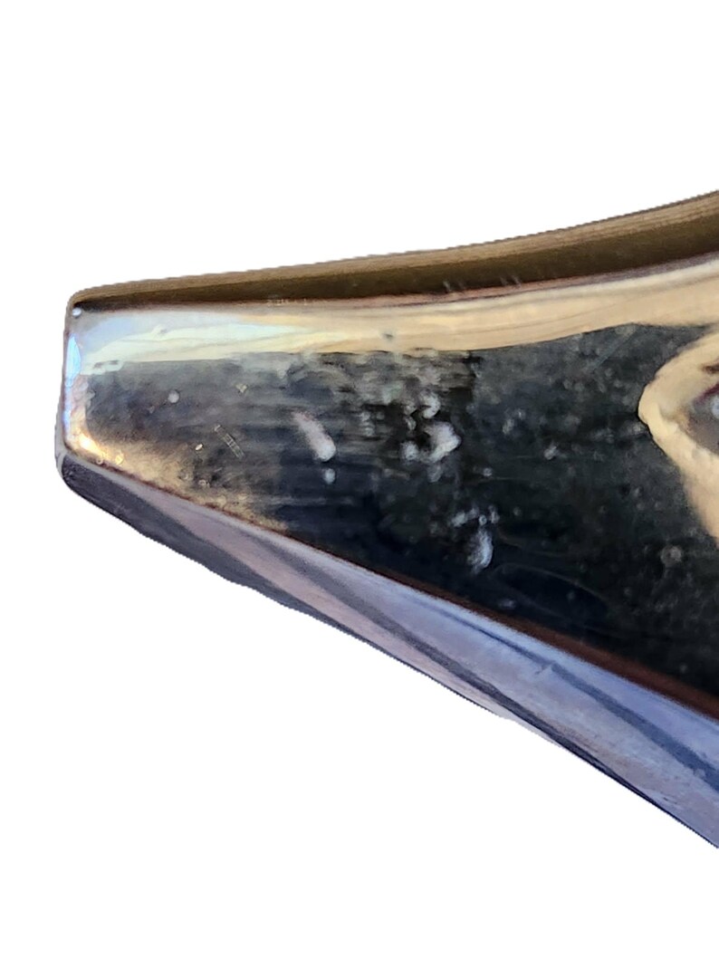 May include: Close-up of a shiny, metallic object with a reflective surface. The object has a dark, possibly blue or black, color with a lighter, possibly silver, edge. The surface shows some imperfections.