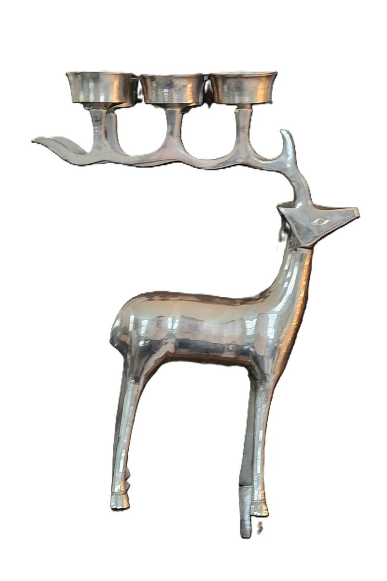 May include: Silver-colored metal deer sculpture with three candle holders on its antlers. The deer has a sleek, modern design, with a polished finish. The sculpture is a decorative item.