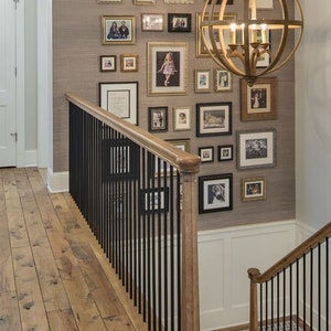 May include: A wooden staircase with a black metal railing leads up to a wall decorated with framed photos and a large, round, gold-toned chandelier.