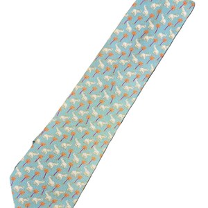 May include: A light blue necktie with a repeating pattern of white elephants and orange palm trees. The tie is made of a smooth fabric and has a classic pointed end.