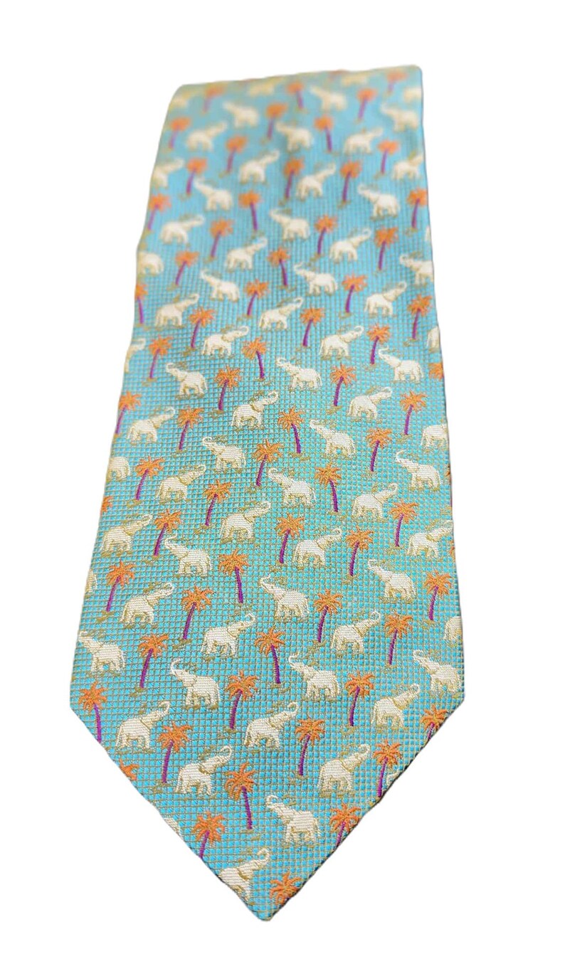 May include: A light blue necktie with a repeating pattern of white elephants and orange palm trees. The tie has a textured appearance and a classic pointed end. A stylish accessory for any wardrobe.