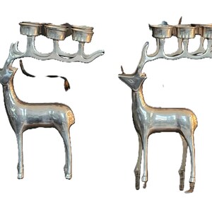 May include: Two silver-colored reindeer candle holders. Each reindeer has a rack of antlers that hold four candle cups. The reindeer are standing upright with their heads held high. The candle holders are a festive decoration.