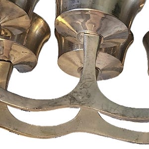 May include: Close-up of a vintage brass candelabra. The candelabra features multiple candle holders with a curved, decorative base. The brass has a tarnished appearance, suggesting age and use. The design is ornate and likely for decorative purposes.