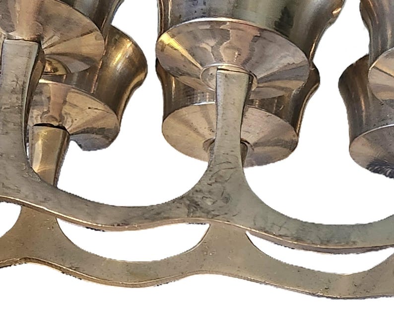 May include: Close-up of a vintage brass candelabra. The candelabra features multiple candle holders with a curved, decorative base. The brass has a tarnished appearance, suggesting age and use. The design is ornate and likely for decorative purposes.