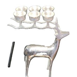 May include: A silver-colored deer-shaped candle holder with six small cup-shaped candle holders on its antlers. A black, rectangular object is next to the deer. The deer has a polished, metallic finish.