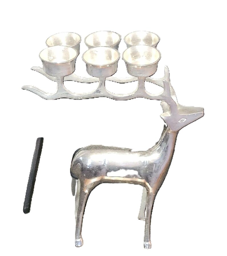 May include: A silver-colored deer-shaped candle holder with six small cup-shaped candle holders on its antlers. A black, rectangular object is next to the deer. The deer has a polished, metallic finish.