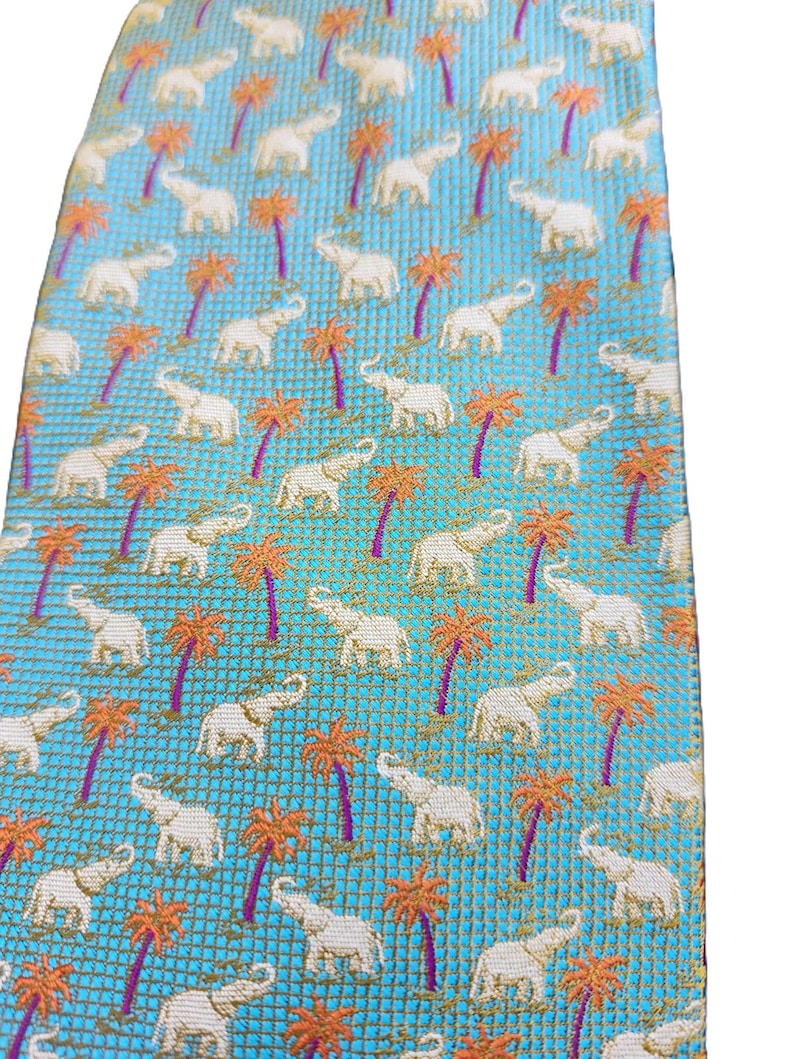 May include: A light blue tie with a repeating pattern of white elephants and orange palm trees. The tie has a textured weave and a classic shape, suitable for formal or semi-formal occasions.