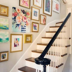 Puede incluir: Una escalera blanca con una barandilla negra y una pared decorada con una galer&iacute;a de obras de arte enmarcadas en marcos dorados. Las obras de arte incluyen pinturas abstractas, estampados florales y paisajes.