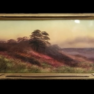 May include: A rectangular landscape painting in a gold-toned frame featuring a hazy sunset over a rolling hill with dark green trees, patches of reddish-brown foliage, and a soft yellow sky. A signature is visible in the bottom left corner.