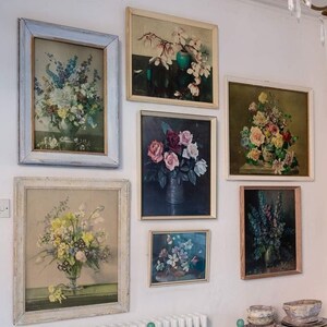 May include: A wall gallery of framed floral prints in various sizes and styles. The prints feature different types of flowers, including roses, lilies, and magnolias. The frames are all white or cream-colored and have a simple, elegant design.