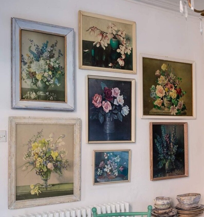 May include: A wall gallery of framed floral prints in various sizes and styles. The prints feature different types of flowers, including roses, lilies, and magnolias. The frames are all white or cream-colored and have a simple, elegant design.