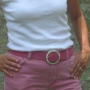 Puede incluir: Un cintur&oacute;n rosa con una hebilla plateada grande con un c&iacute;rculo de diamantes de imitaci&oacute;n. El cintur&oacute;n se lleva sobre unos vaqueros rosas.