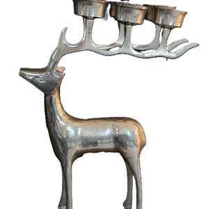 May include: Silver-colored deer-shaped candle holder. The deer has a slender body and long legs, with a rack of antlers that hold four candle cups. The candle holder is made of metal and has a reflective surface.