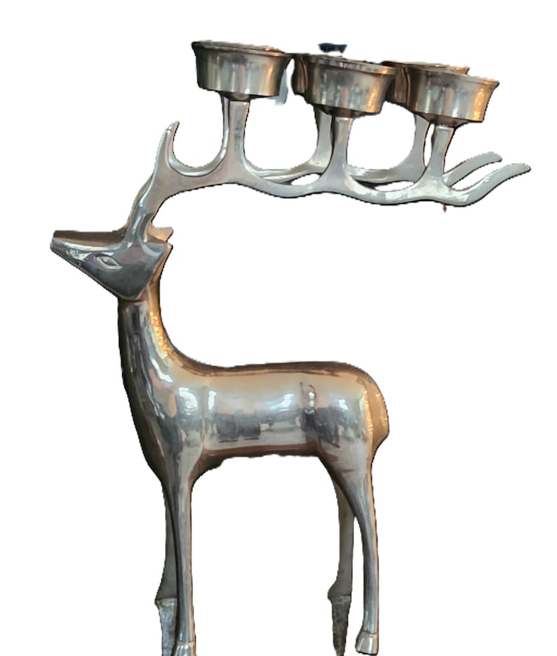 May include: Silver-colored deer-shaped candle holder. The deer has a slender body and long legs, with a rack of antlers that hold four candle cups. The candle holder is made of metal and has a reflective surface.