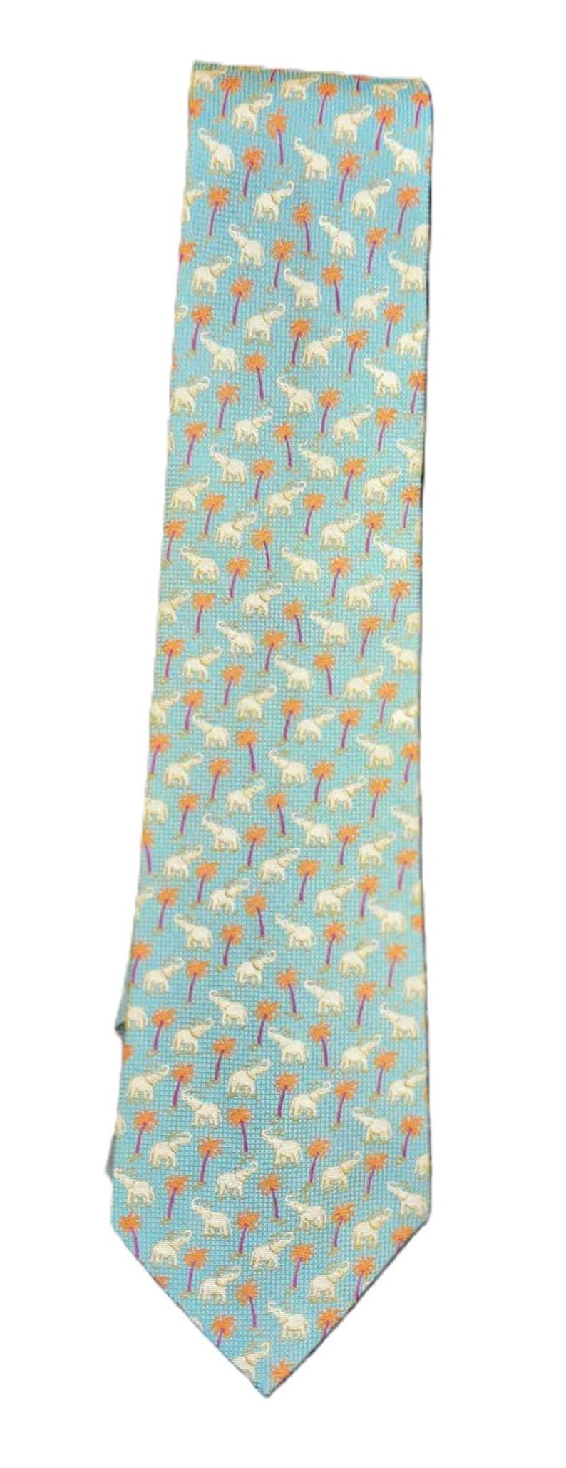 May include: A light blue necktie with a repeating pattern of white elephants and orange palm trees. The tie is a standard length and width, suitable for formal or business attire.