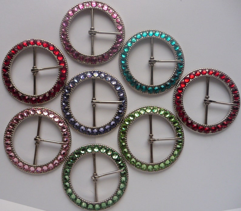 Puede incluir: Surtido de ocho hebillas redondas de cintur&oacute;n de metal con diferentes colores de piedras de imitaci&oacute;n. Las hebillas son todas del mismo tama&ntilde;o y tienen un acabado plateado.