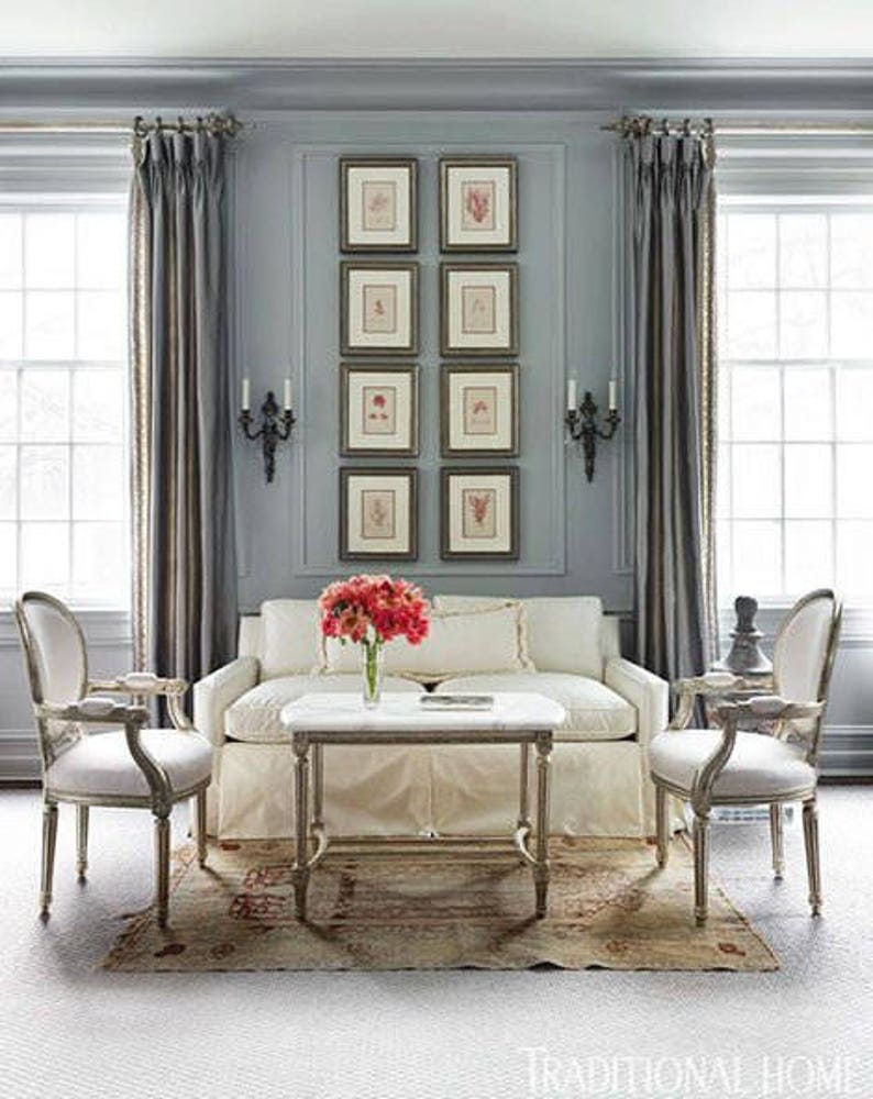 Handsome example of a vertical display of eight botanical prints arranged in two vertical columns on a gray wall between two tall windows with drapes. Dark wood frames with cream colored mats. Black double sconces on each side of the display.