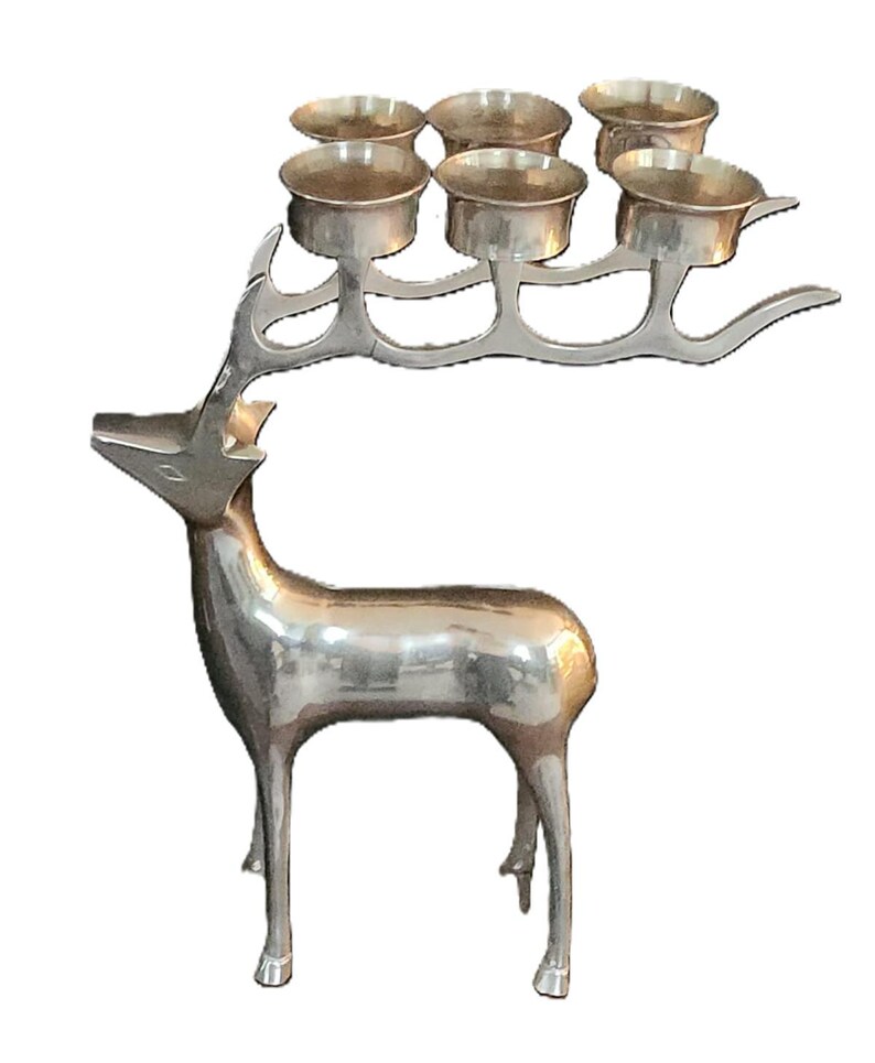 May include: A silver-colored metal deer sculpture with six candle holders on its antlers. The deer is standing, with a polished finish, and the candle holders are small, round cups.