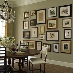 May include: A dining room with a round wooden table and chairs. The wall is decorated with a gallery wall of framed artwork in various sizes and styles.