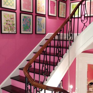May include: A pink staircase with a black wrought iron railing. The wall is decorated with framed artwork featuring colourful patterns. The text on one of the frames reads "You were up side down It's a party in floral!"