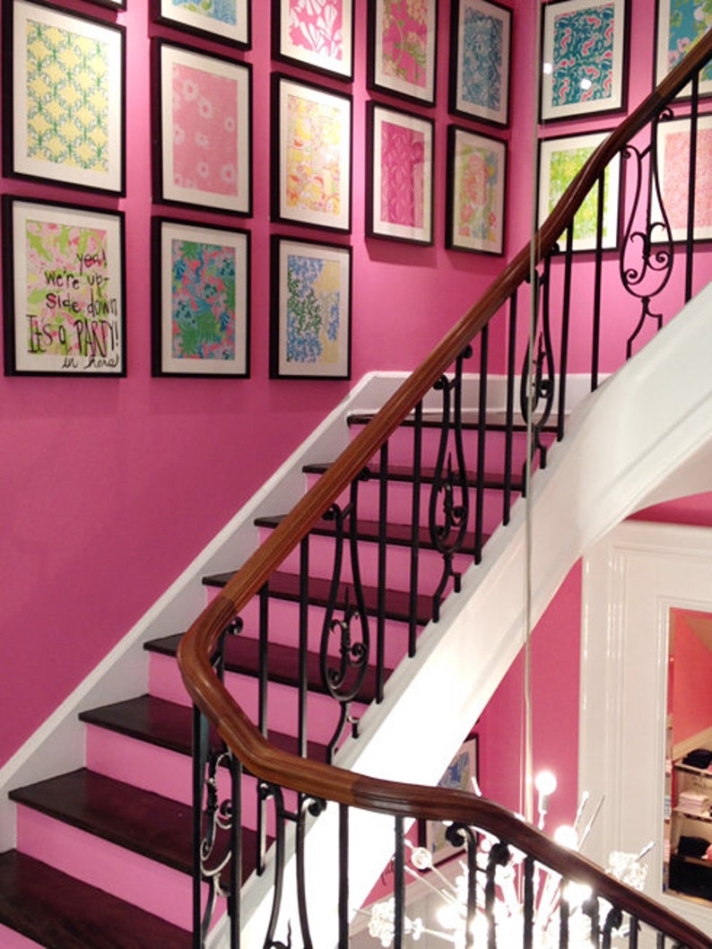 May include: A pink staircase with a black wrought iron railing. The wall is decorated with framed artwork featuring colourful patterns. The text on one of the frames reads "You were up side down It's a party in floral!"