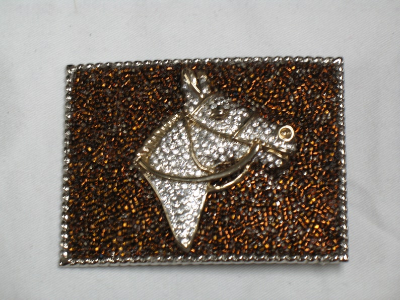 Puede incluir: Un broche de cabeza de caballo de plata y oro con un fondo de cuentas marrones. La cabeza de caballo est&aacute; decorada con diamantes de imitaci&oacute;n.