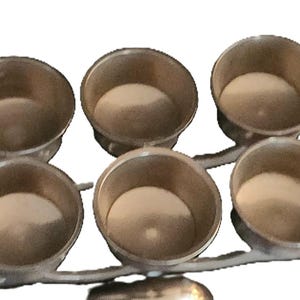 May include: A silver-toned metal serving piece with six small, round bowls. The bowls are arranged in two rows of three, connected by a branching stem. The interior of each bowl appears to be a light beige color.