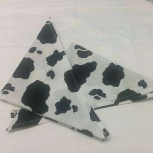 May include: Two black and white cow print fabric triangles folded in half. The fabric is white with black spots.